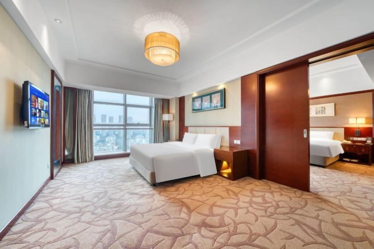 A hotel room with a large bed, a desk, a chair, a television, and a window with a city view.