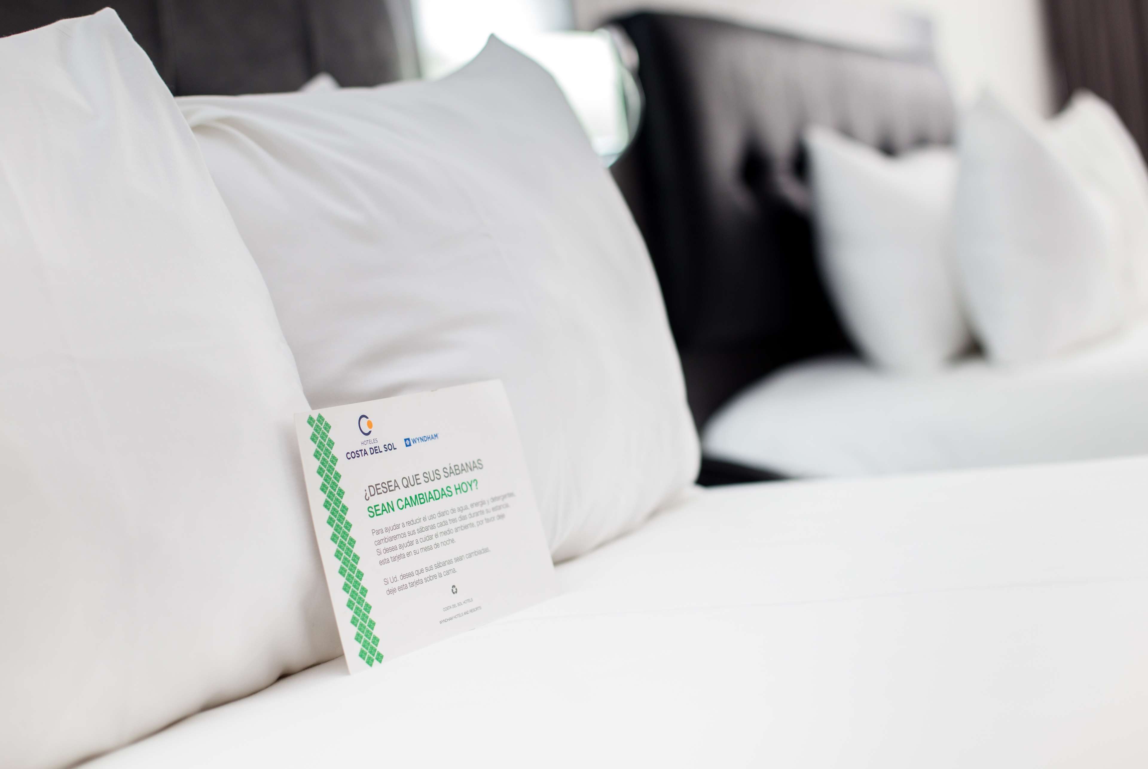 A hotel bed with white bedding and a sign on the pillow.