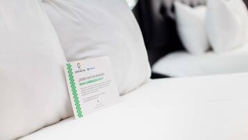 A hotel bed with white bedding and a sign on the pillow.