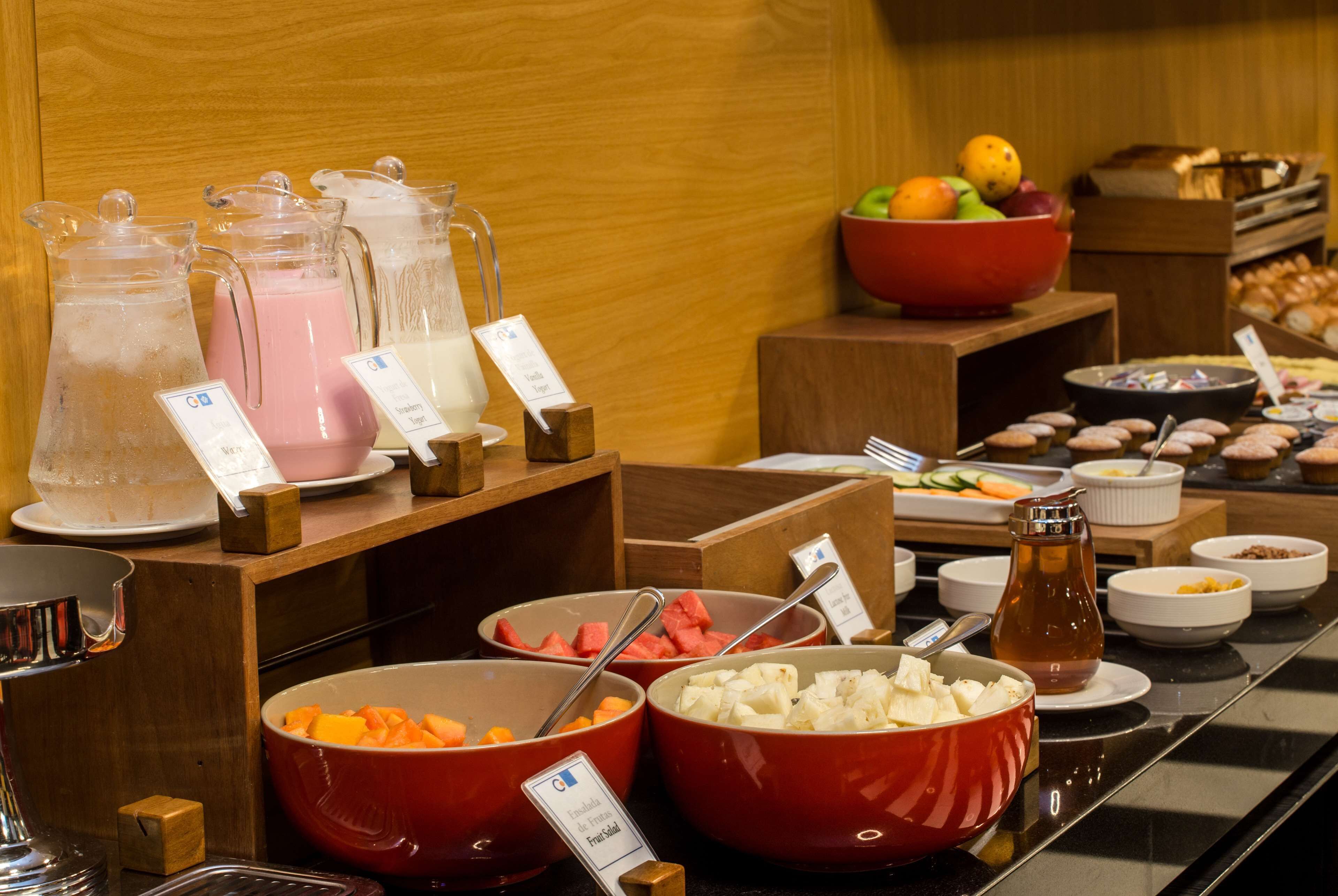 A buffet with various food items and beverages, including bowls of fruits, vegetables, and a pitcher of juice.