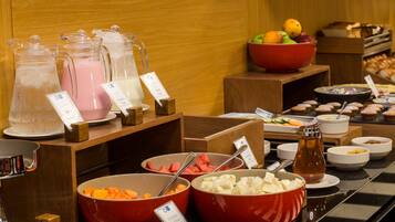 A buffet with various food items and beverages, including bowls of fruits, vegetables, and a pitcher of juice.
