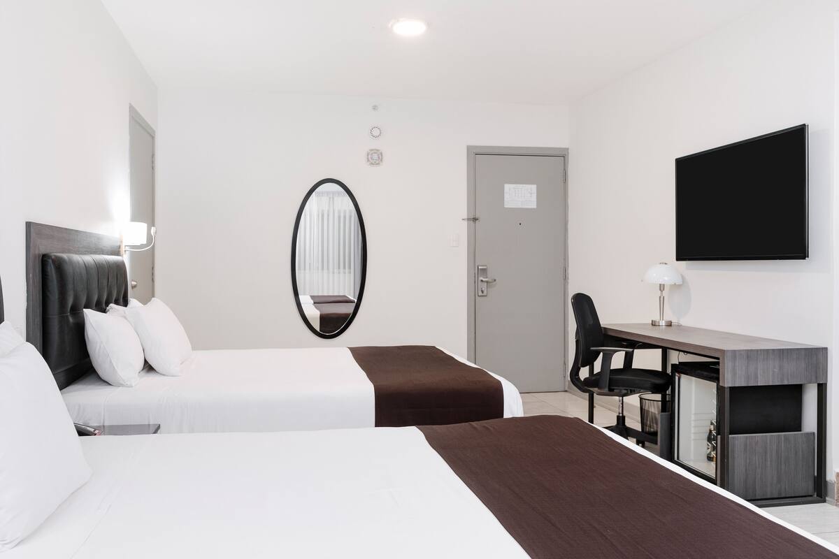 Una habitación de hotel con dos camas, un escritorio, una silla, un televisor y un espejo.