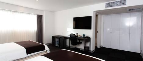 Una habitación de hotel con cama, escritorio, silla, televisor y armario.
