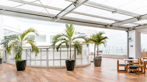 A spacious indoor area with wooden flooring, potted palm trees, and a seating area with wooden chairs. - Wyndham Costa del Sol Tumbes (Tumbes)