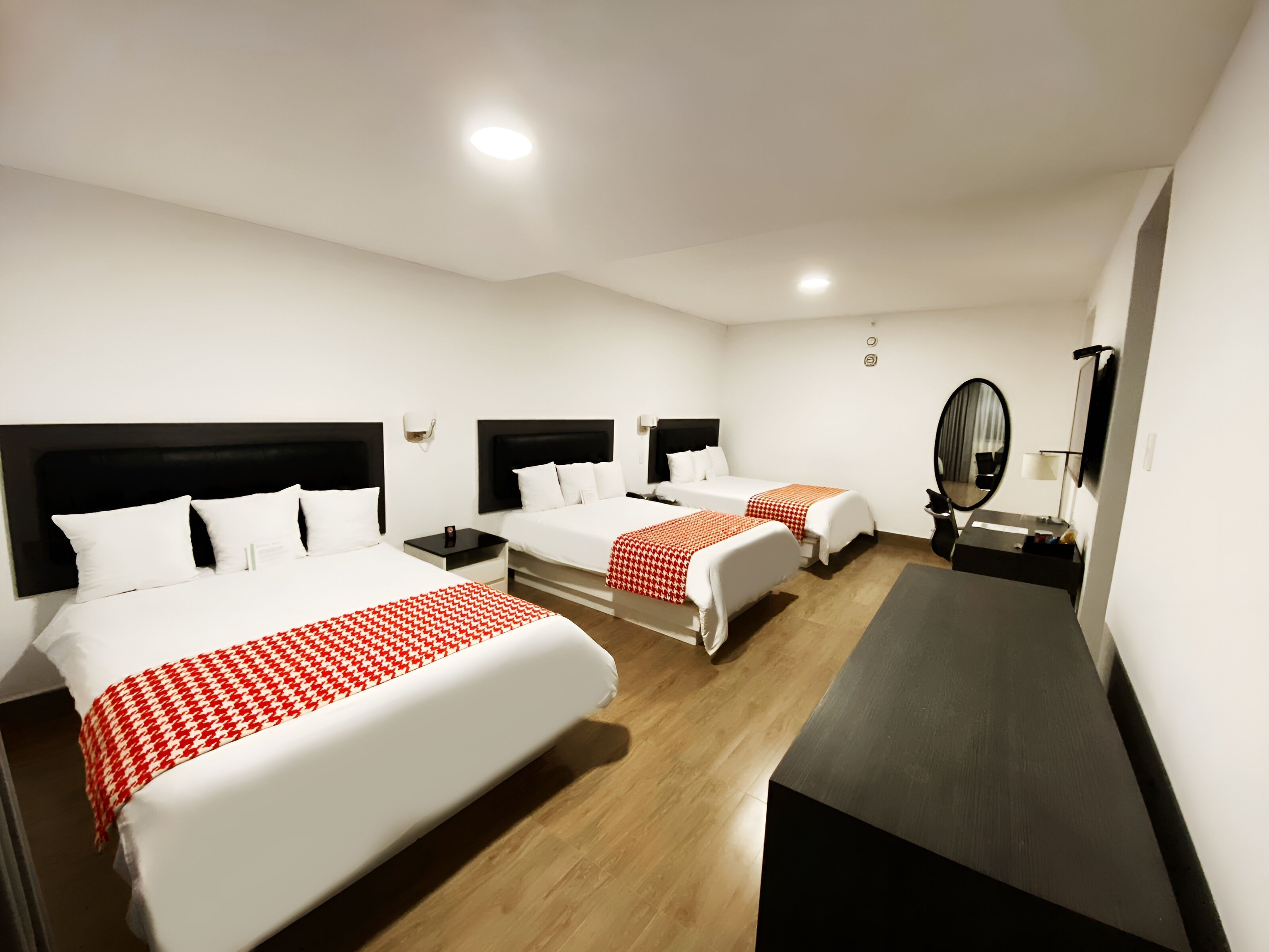 Ein Hotelzimmer mit drei Betten, einem Schreibtisch, einem Spiegel und einem kleinen Tisch.