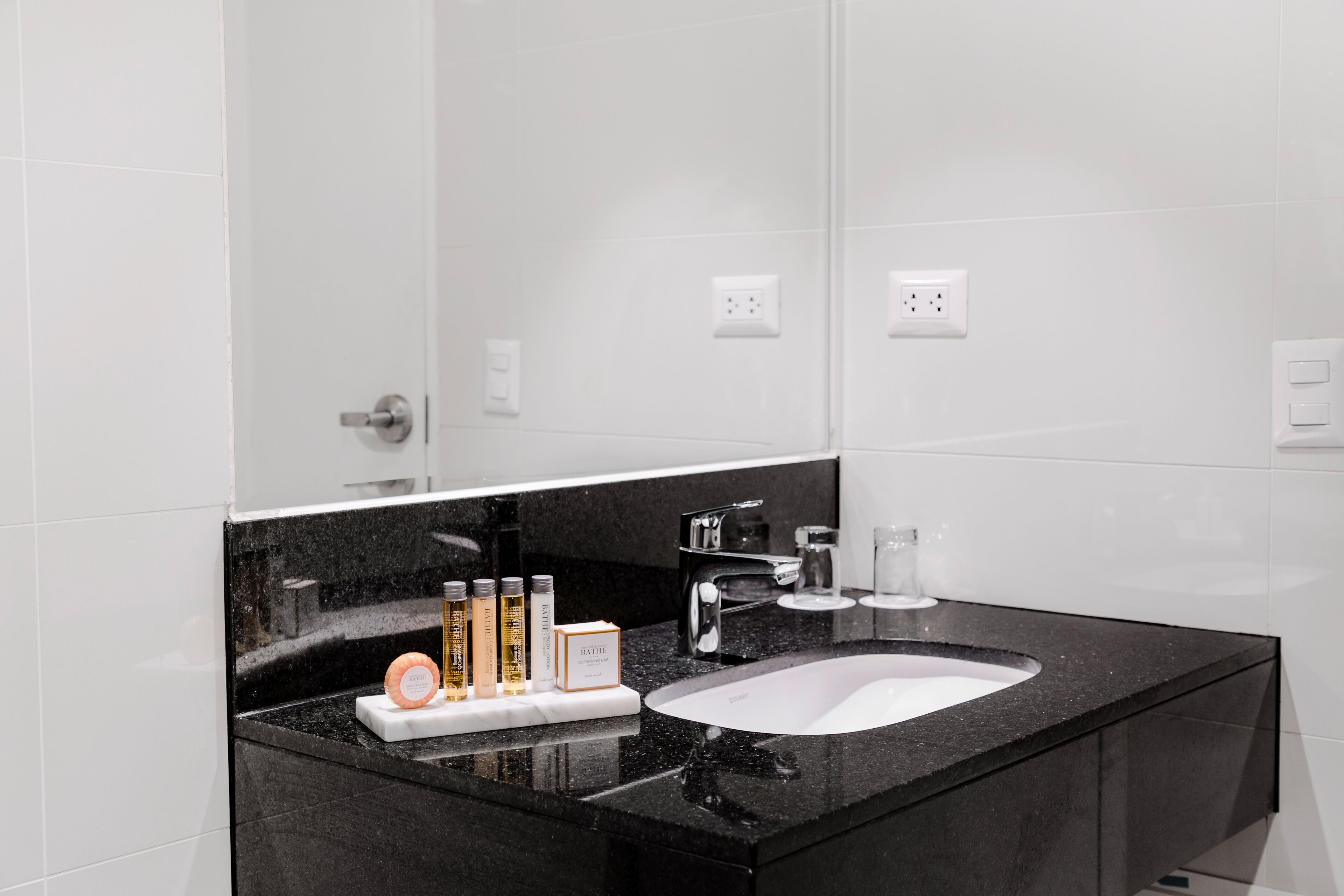 Un baño moderno con encimera de granito negro, un lavamanos blanco y un espejo grande.