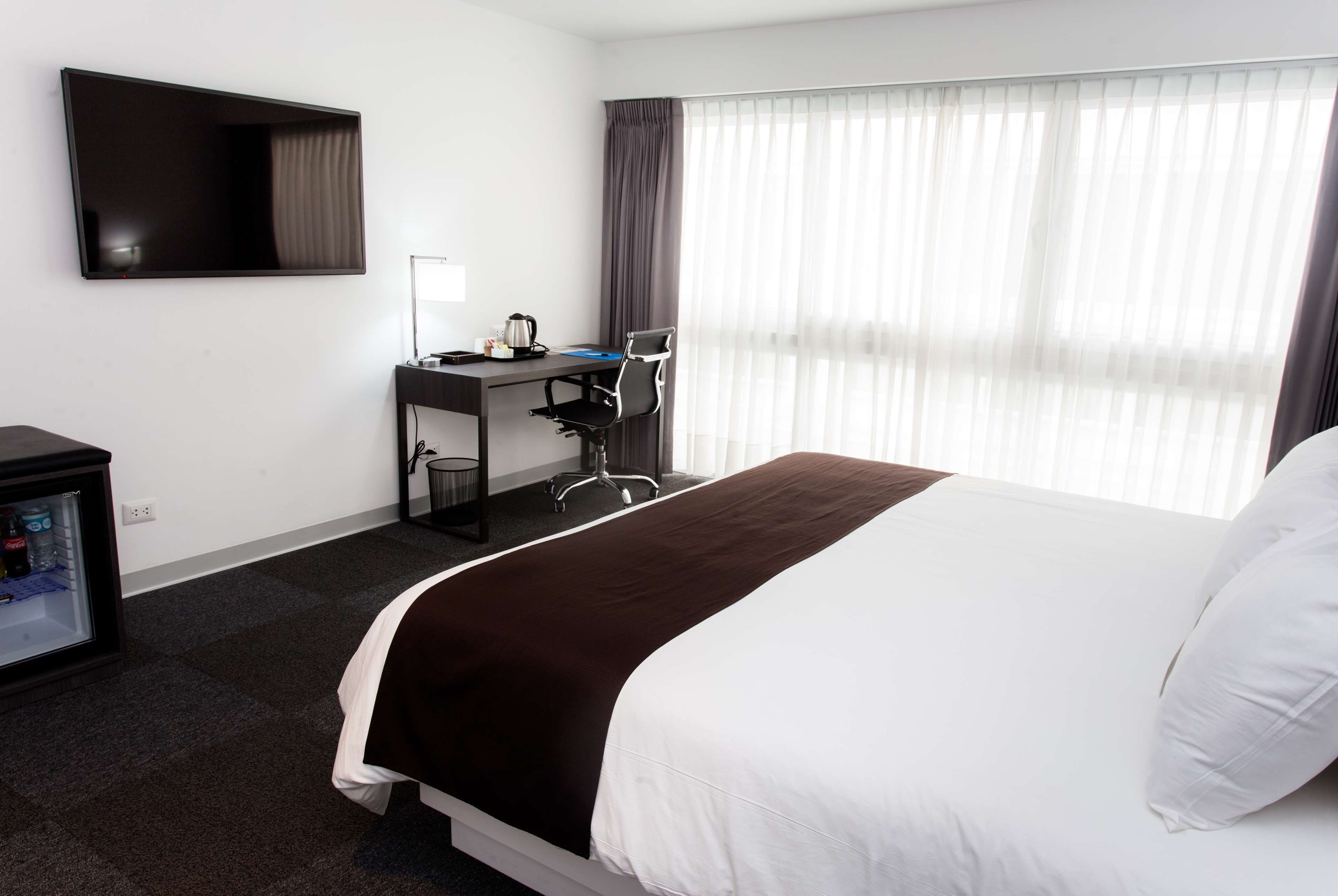 A hotel room with a bed, a desk, a chair, a television, and a window with curtains.