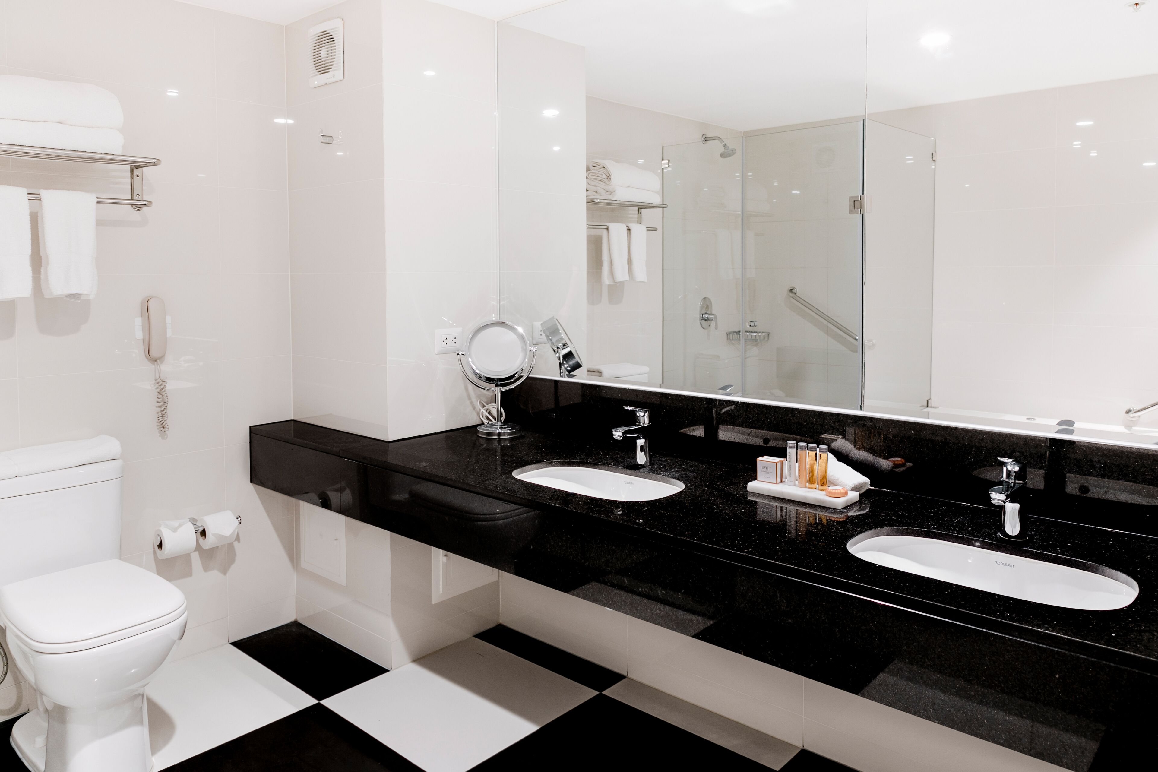 Un baño moderno con encimera negra, dos lavabos, un espejo grande y una cabina de ducha de vidrio.