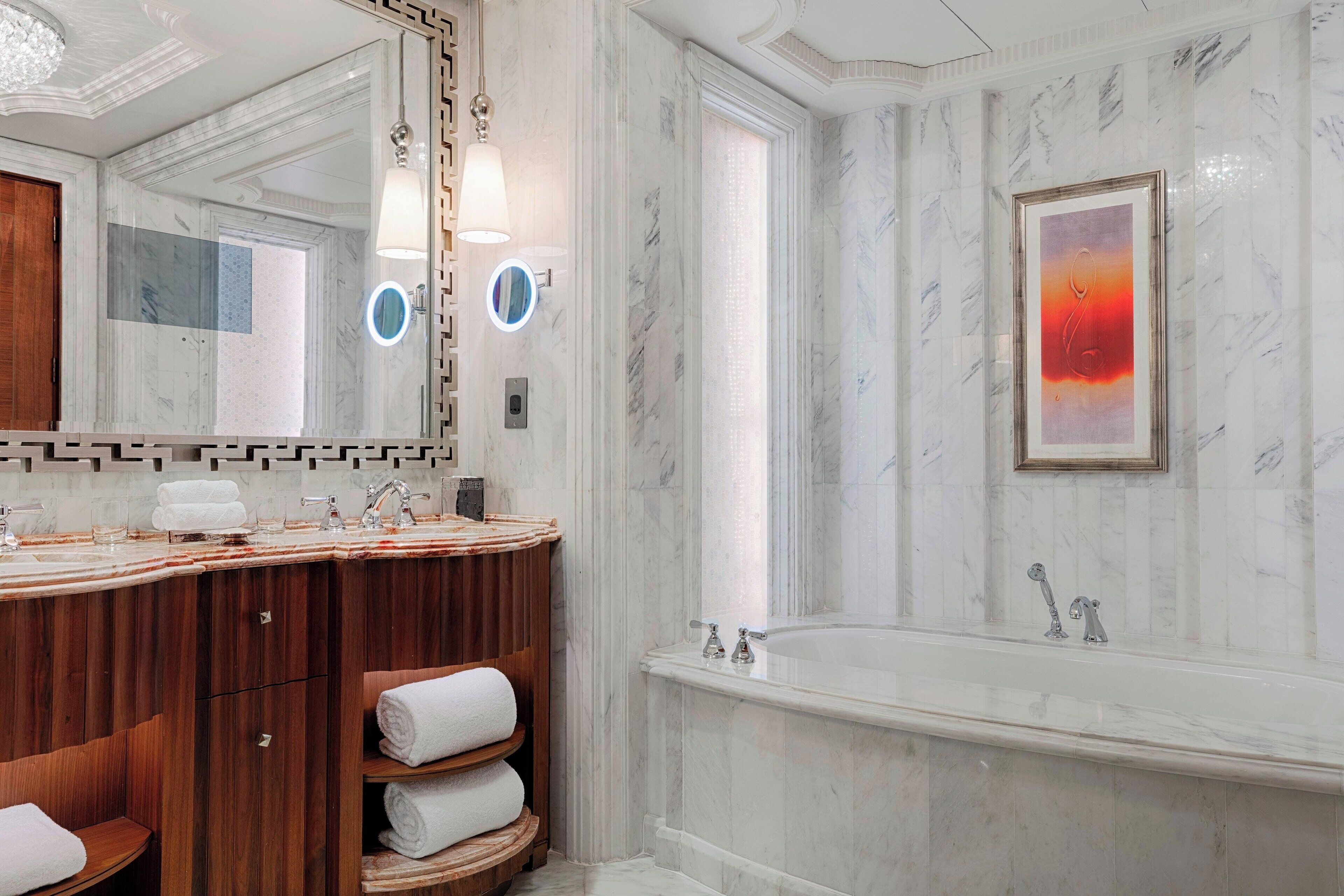 A luxurious bathroom with a marble vanity, a large bathtub, and a framed artwork on the wall.