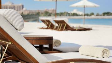 Un espace de détente aménagé sur la plage, avec des chaises longues en bois, des serviettes blanches et des parasols.
