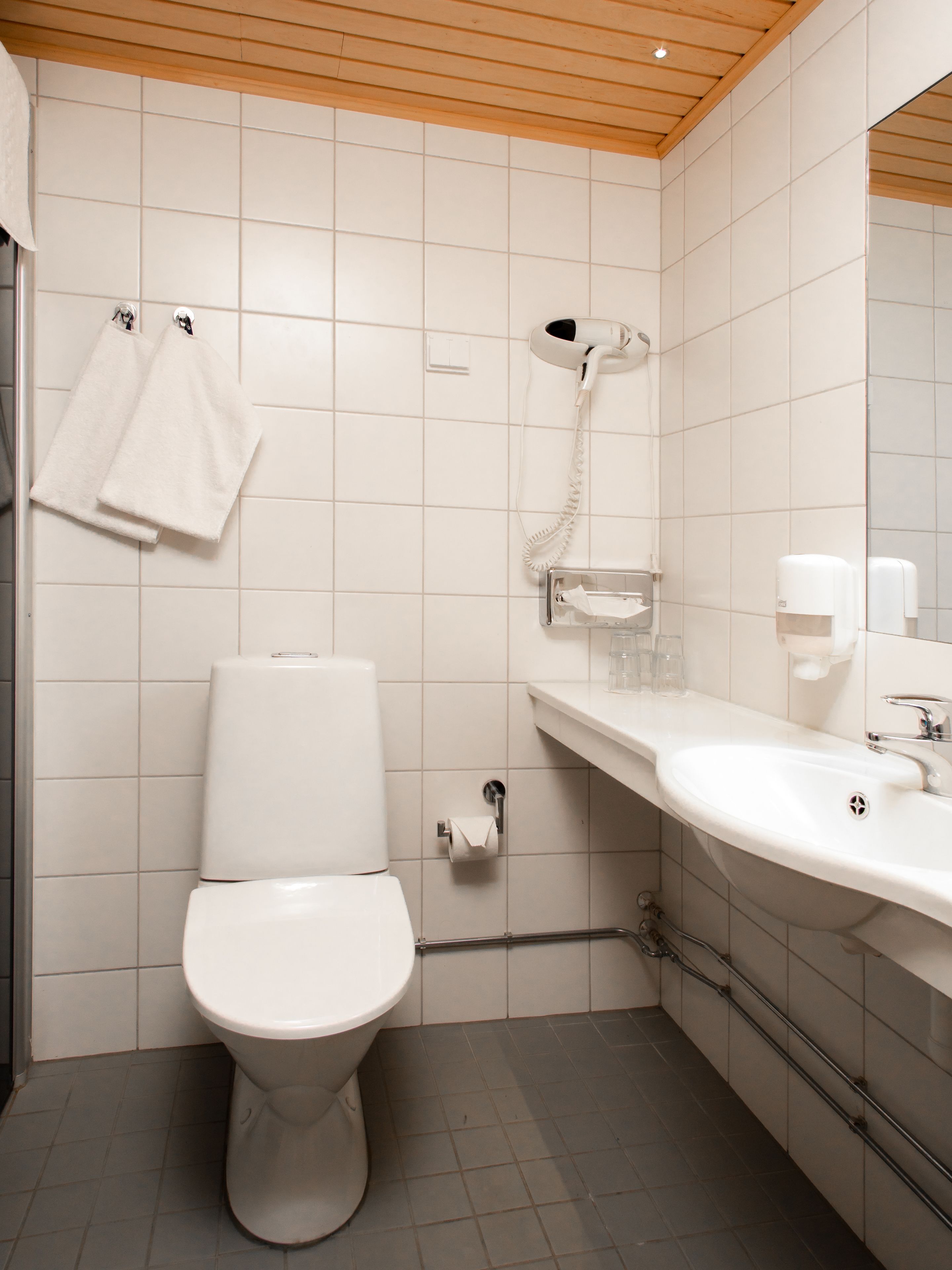 A modern bathroom with a white toilet, a sink, and a hairdryer mounted on the wall.