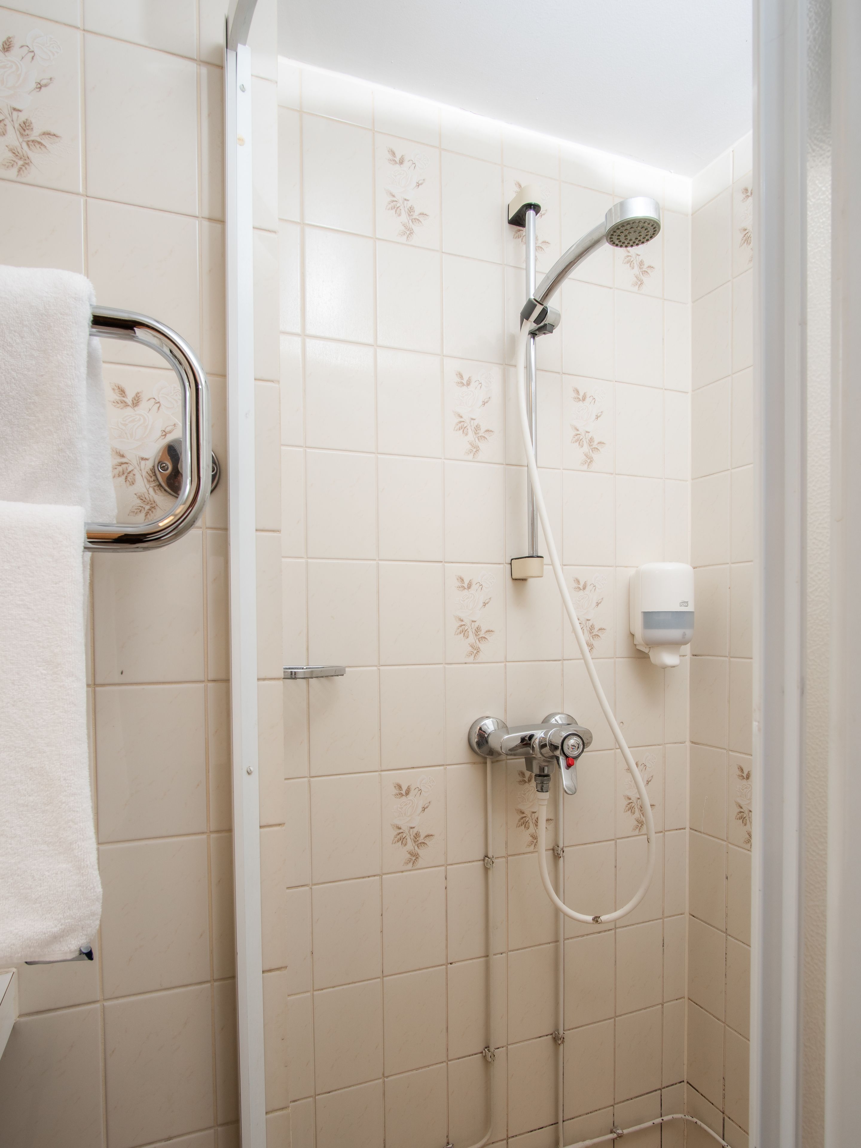 A shower with a handheld showerhead, a wall-mounted faucet, and a handheld showerhead.