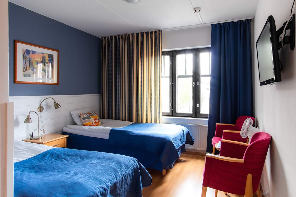Ein Hotelzimmer mit zwei Betten, einem Schreibtisch, einem Sessel, einem Fernseher und einem Fenster mit Vorhängen.