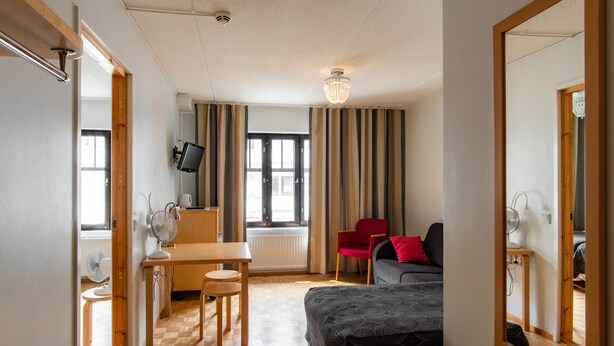 A hotel room with a bed, a desk, a chair, a TV, and a window with curtains. - Hotel Jahtihovi (Kuopio)