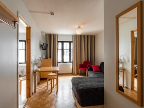 Habitación de hotel con cama, escritorio, silla, televisor y ventana con cortinas.