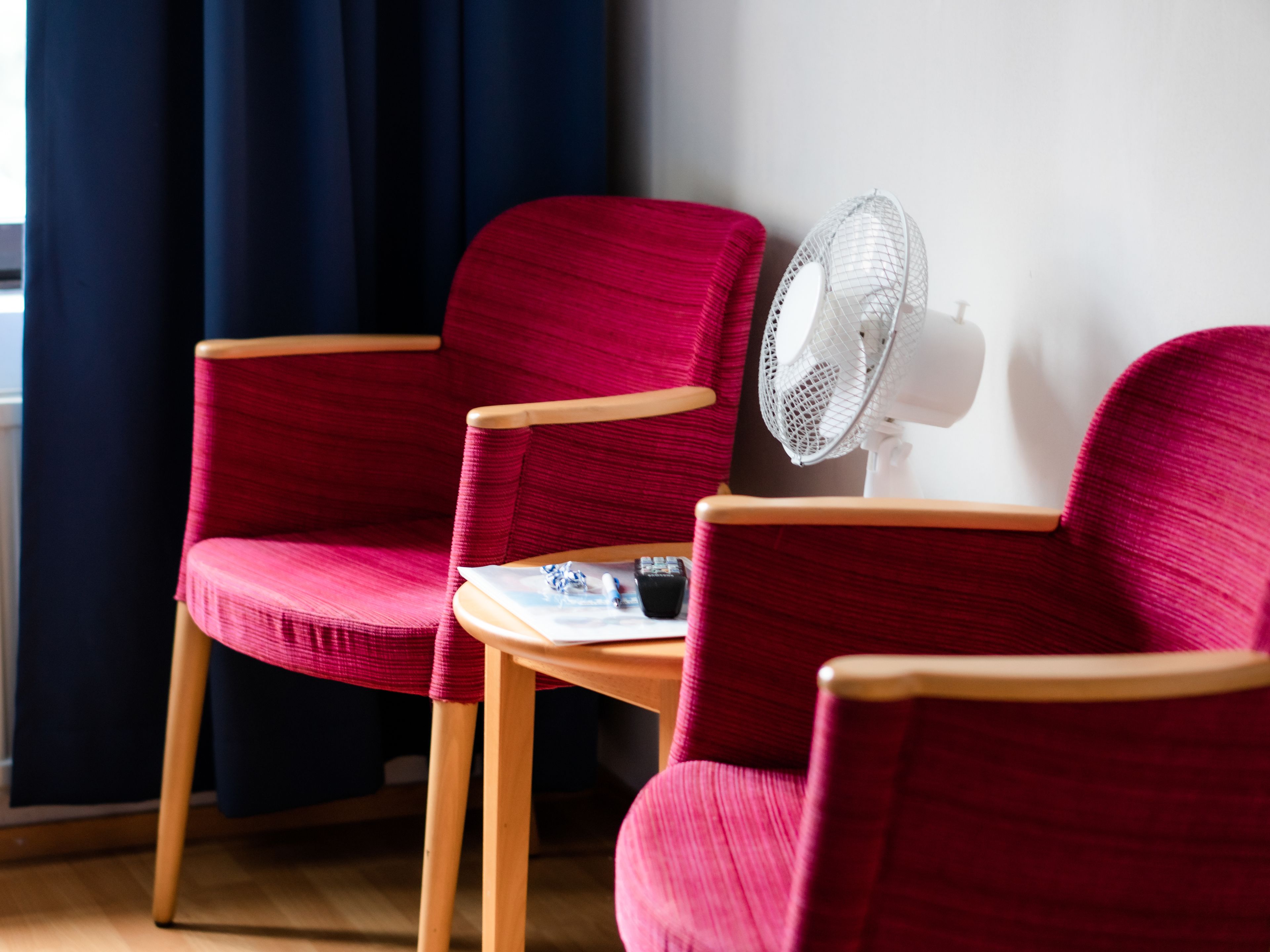 A room with two red armchairs and a small table with a white fan.