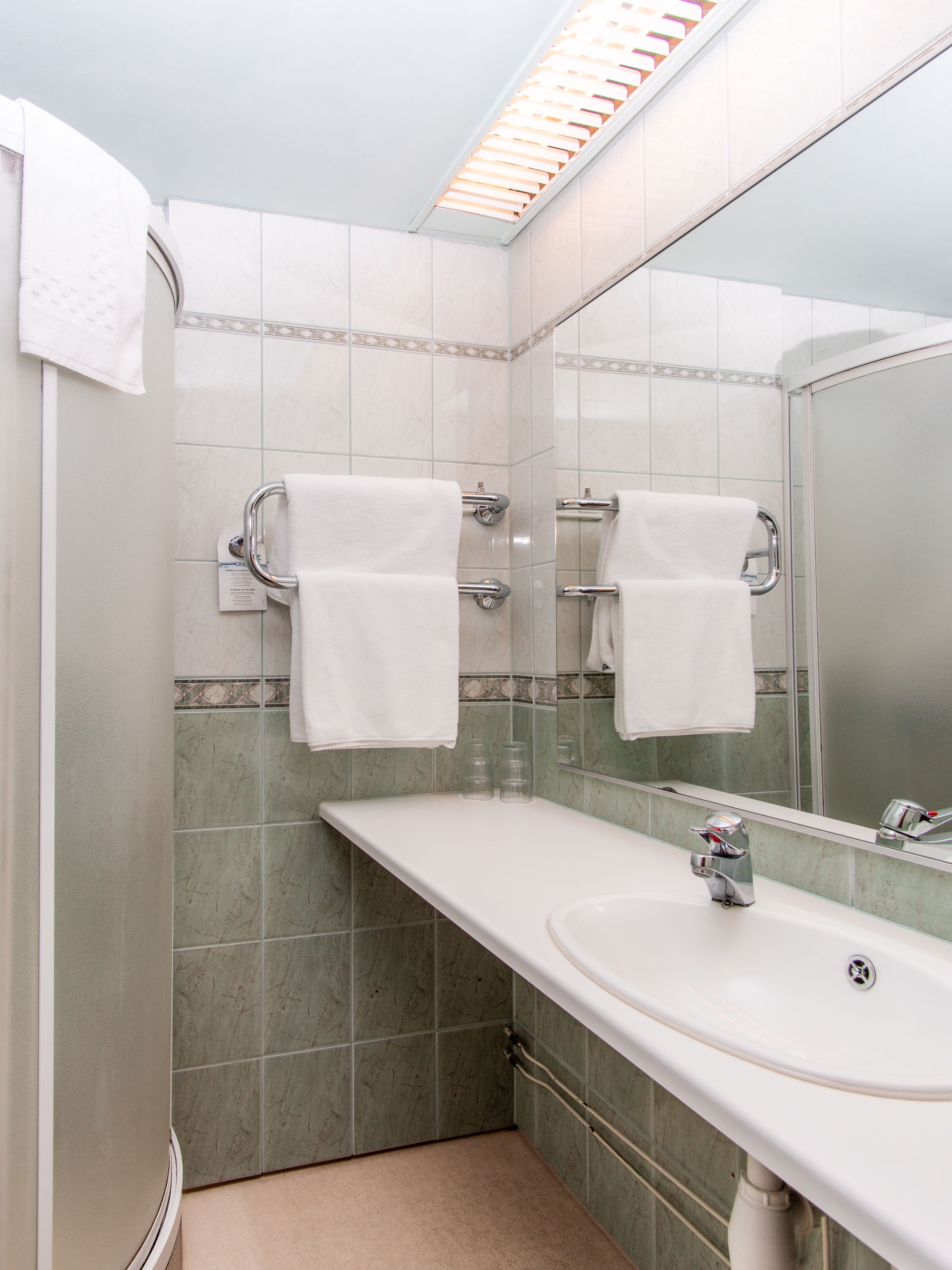 Ein modernes Badezimmer mit einem weißen Waschbecken, zwei Handtuchhaltern, einem Spiegel und grün marmorierten Fliesen.