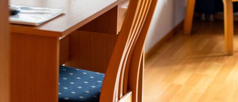 A wooden desk with a lamp, a chair, and a blue sofa in a room with wooden flooring.