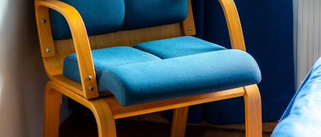 A wooden chair with blue cushions in a room with wooden flooring and a window with blue curtains.