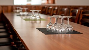 A long wooden table with several empty wine glasses lined up on a black placemat. - Hotel Jahtihovi (Kuopio)