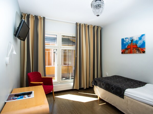 Una habitación de hotel con una cama, un escritorio con control remoto, una silla, un televisor montado en la pared y un cuadro de un edificio.