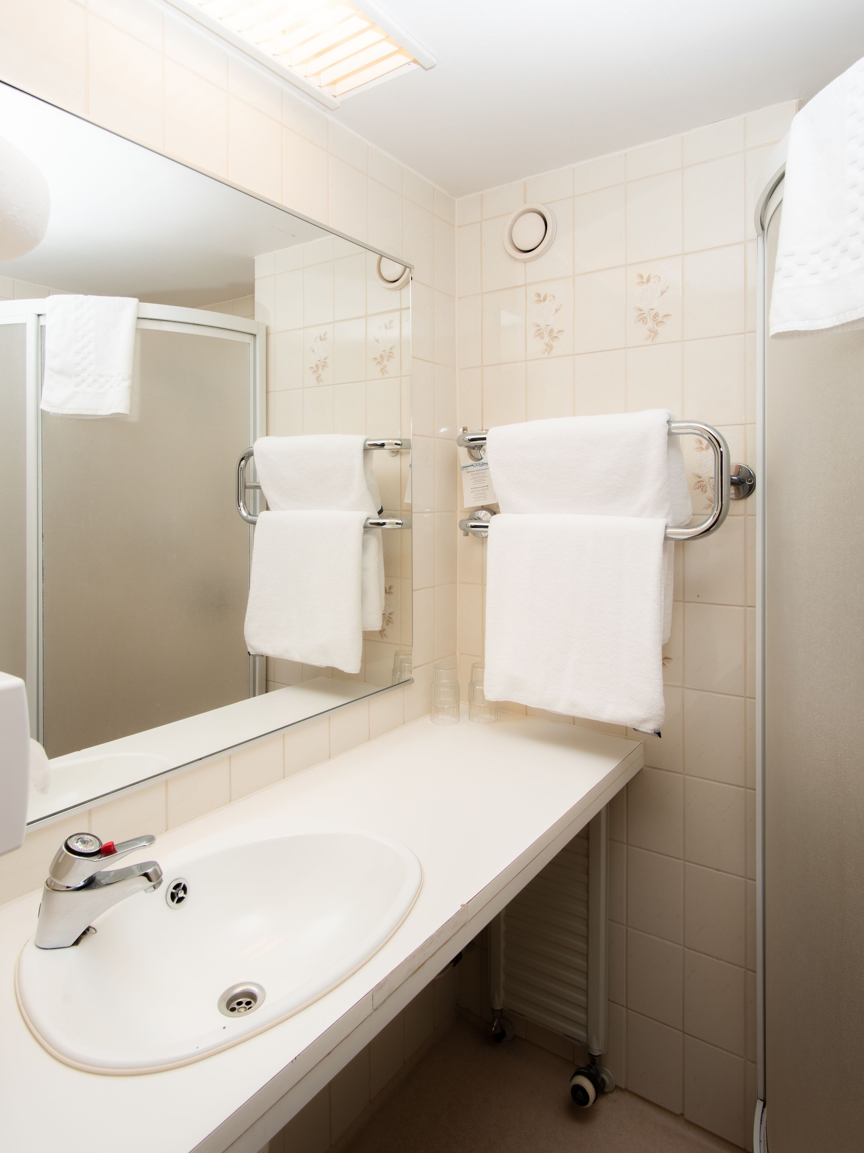 A bathroom with a sink, mirror, towel racks, and a shower.