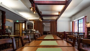A long dining hall with wooden tables and chairs, a high ceiling with exposed beams, and a kitchen area in the background. - Hotel Jahtihovi (Kuopio)