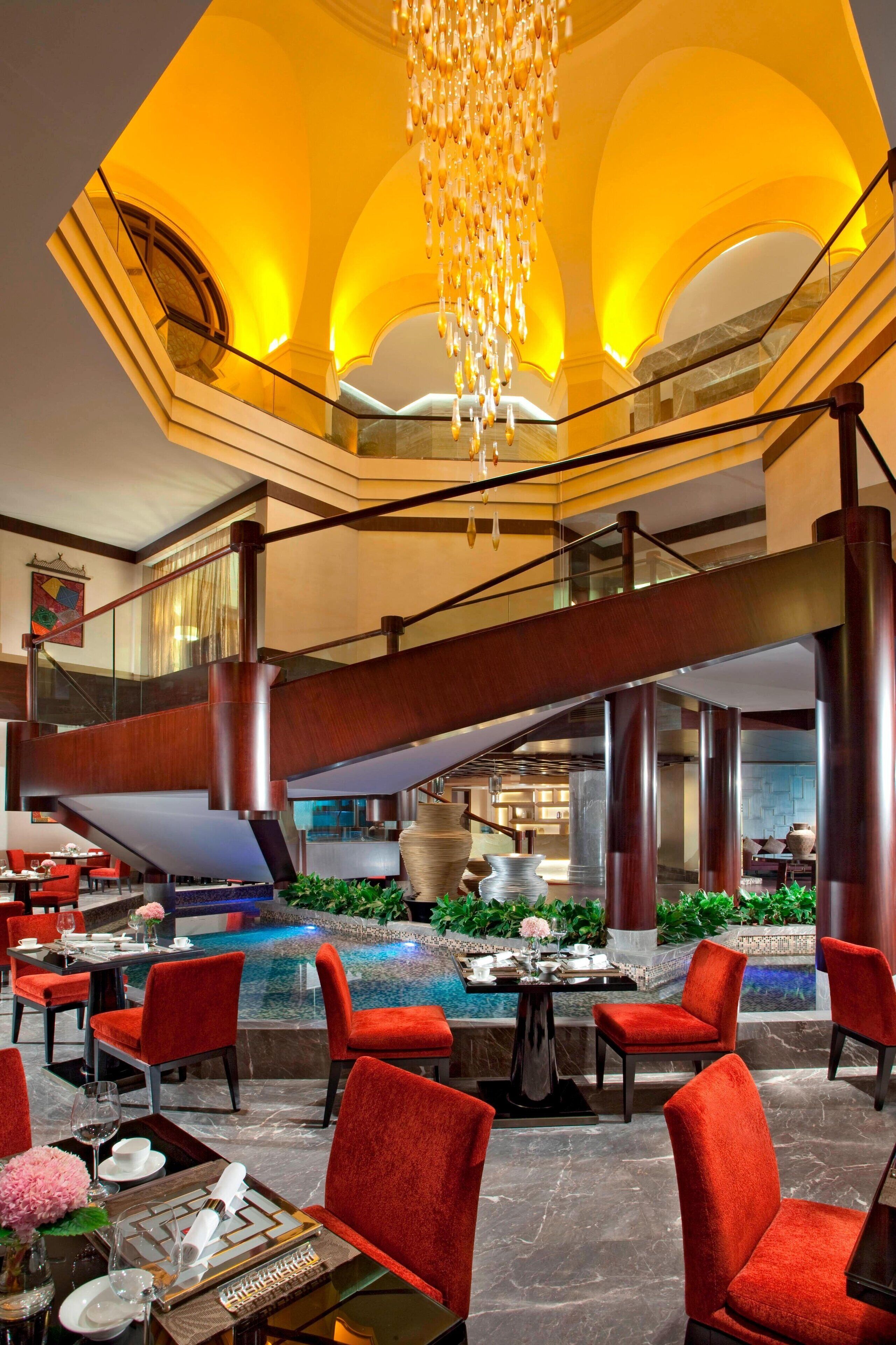 A spacious lobby with a pool, red chairs, and a staircase.