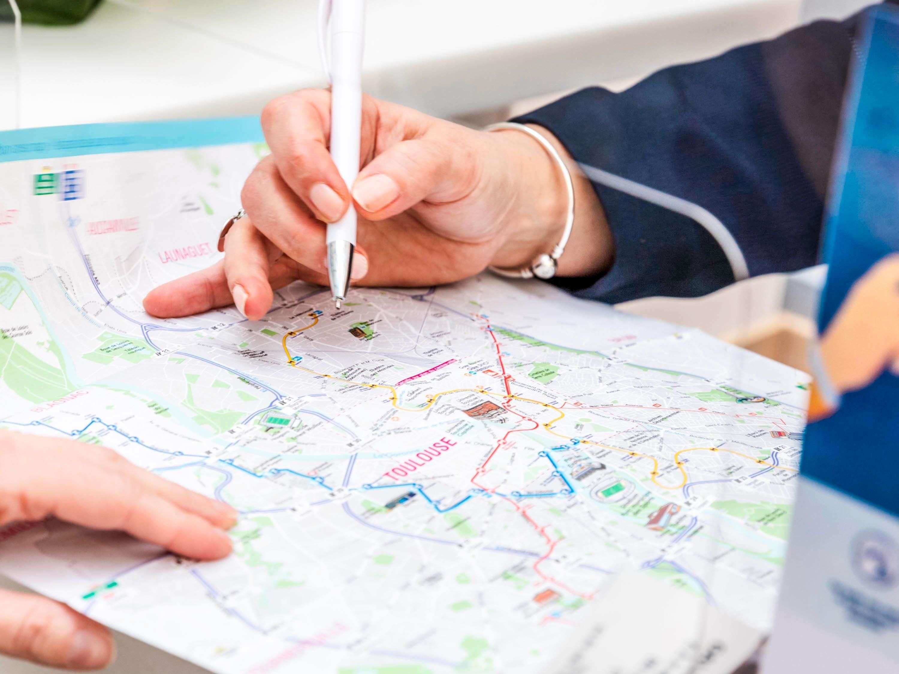 Une personne tenant un stylo, pointant du doigt une carte sur laquelle figurent différentes lignes et étiquettes de couleurs.