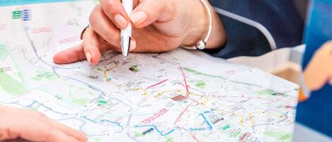 A person holding a pen, pointing at a map with various colored lines and labels.