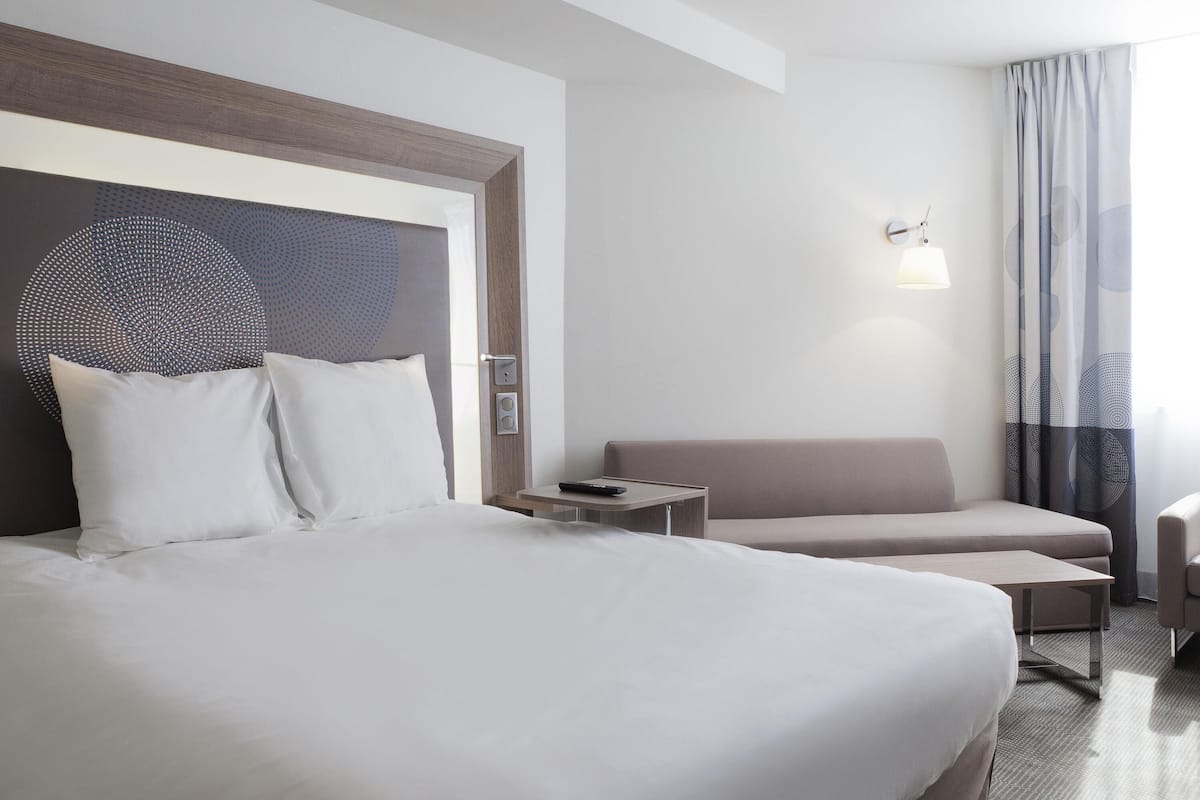 Een hotelkamer met een groot bed, een kleine zithoek, een nachtkastje en een wandlamp.