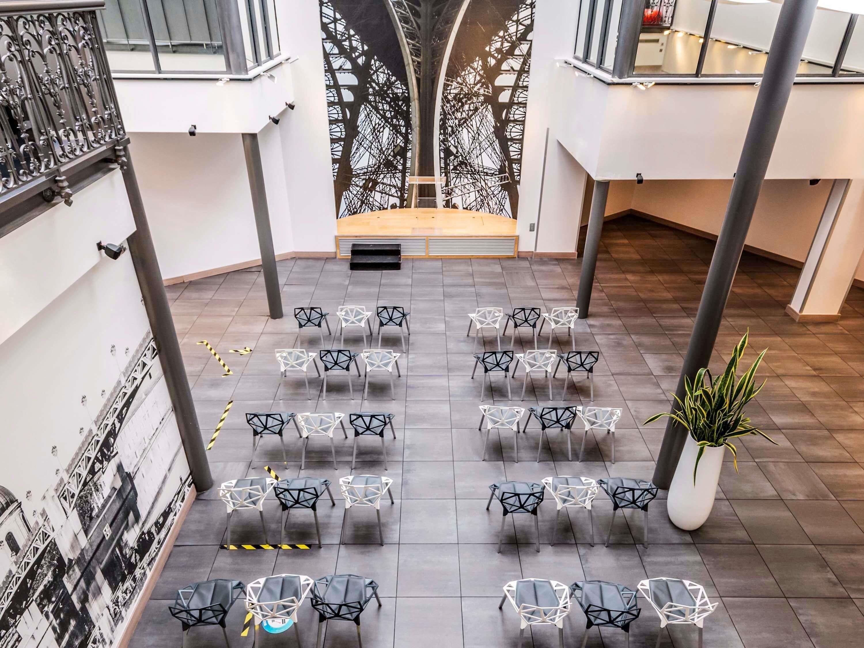 A spacious atrium with a high ceiling, a central staircase, and a seating area with modern chairs arranged in rows.