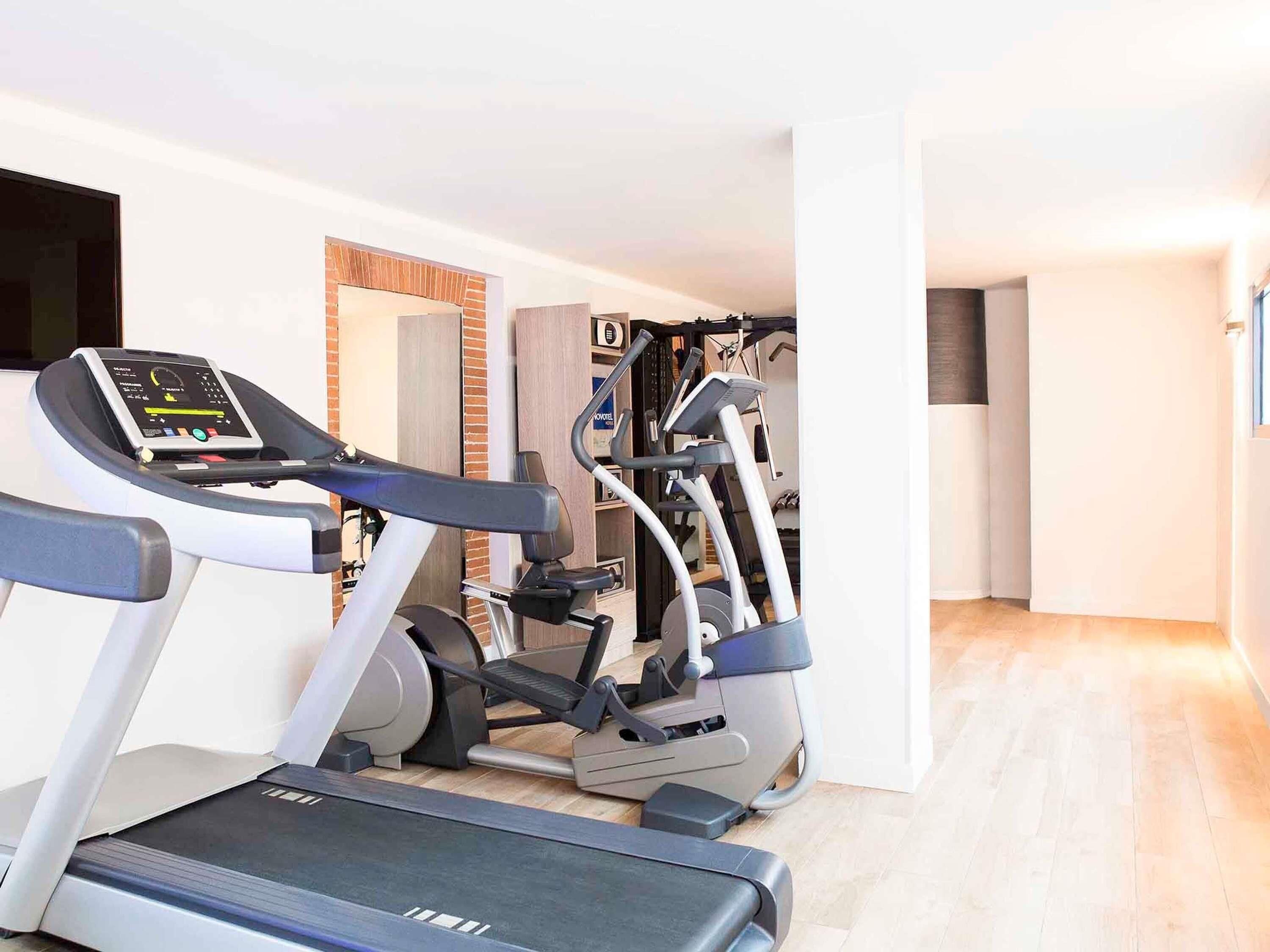 A gym with treadmills and elliptical machines, wooden flooring, and a visible doorway leading to another room.