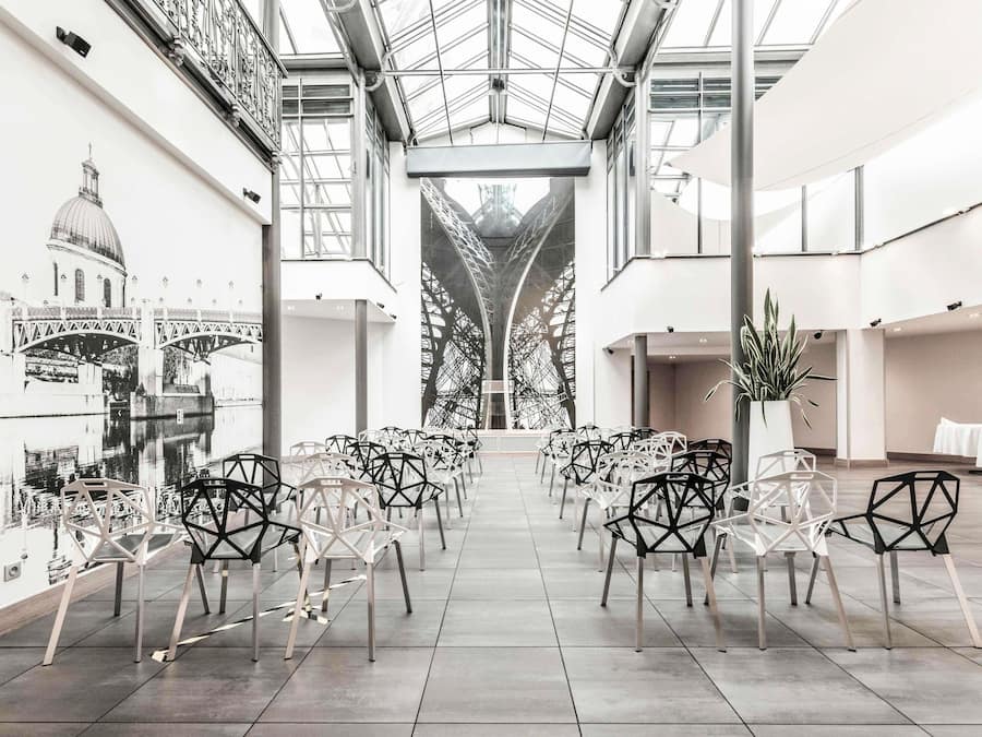 A spacious indoor area with a high ceiling, modern chairs arranged in rows, and a large window overlooking a bridge.