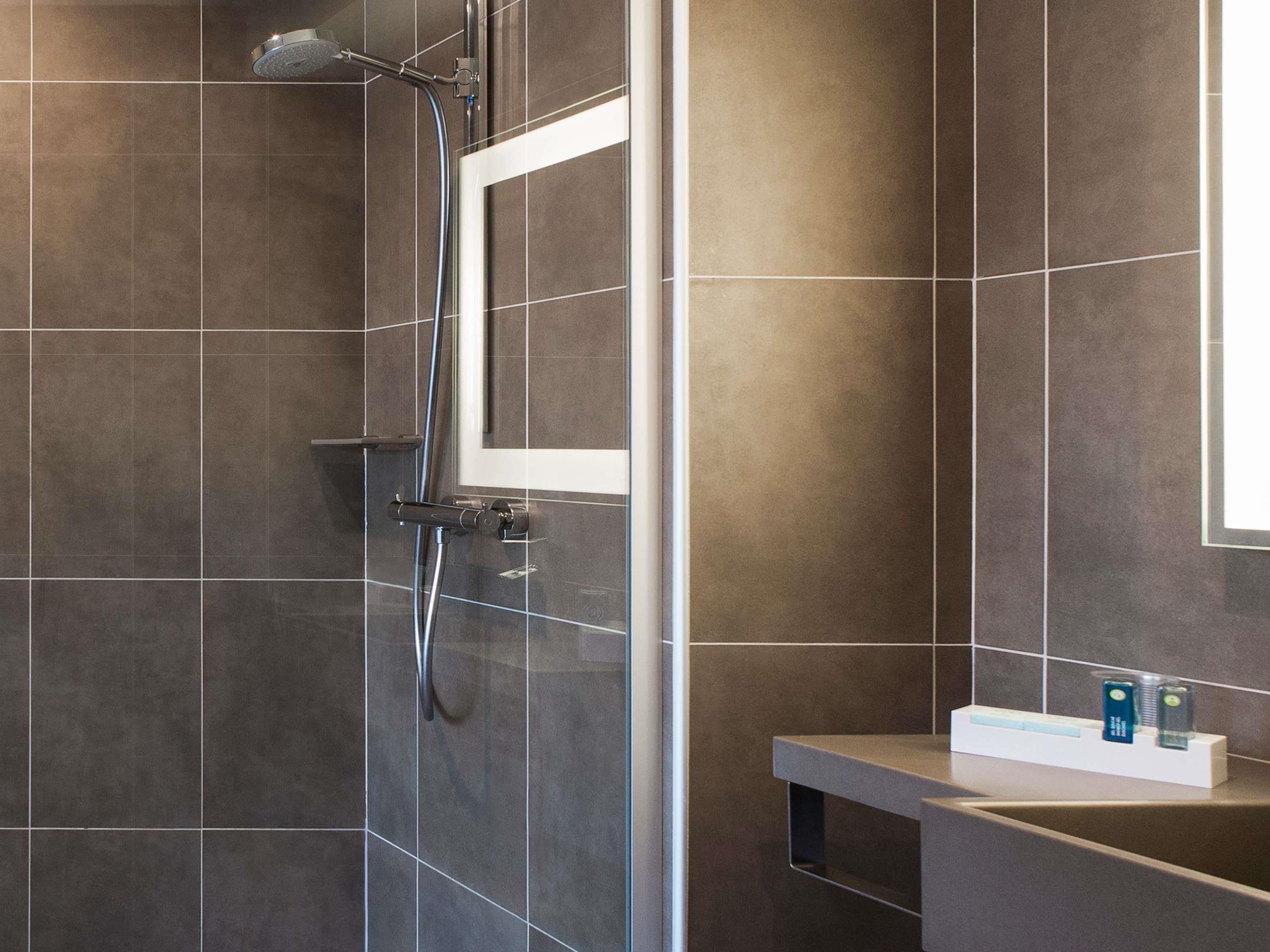 A modern shower with a glass door, a handheld showerhead, and a wall-mounted faucet.