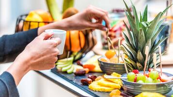 Uma pessoa segurando uma xícara, um prato de frutas com abacaxi e outras frutas, e uma tigela de uvas.
