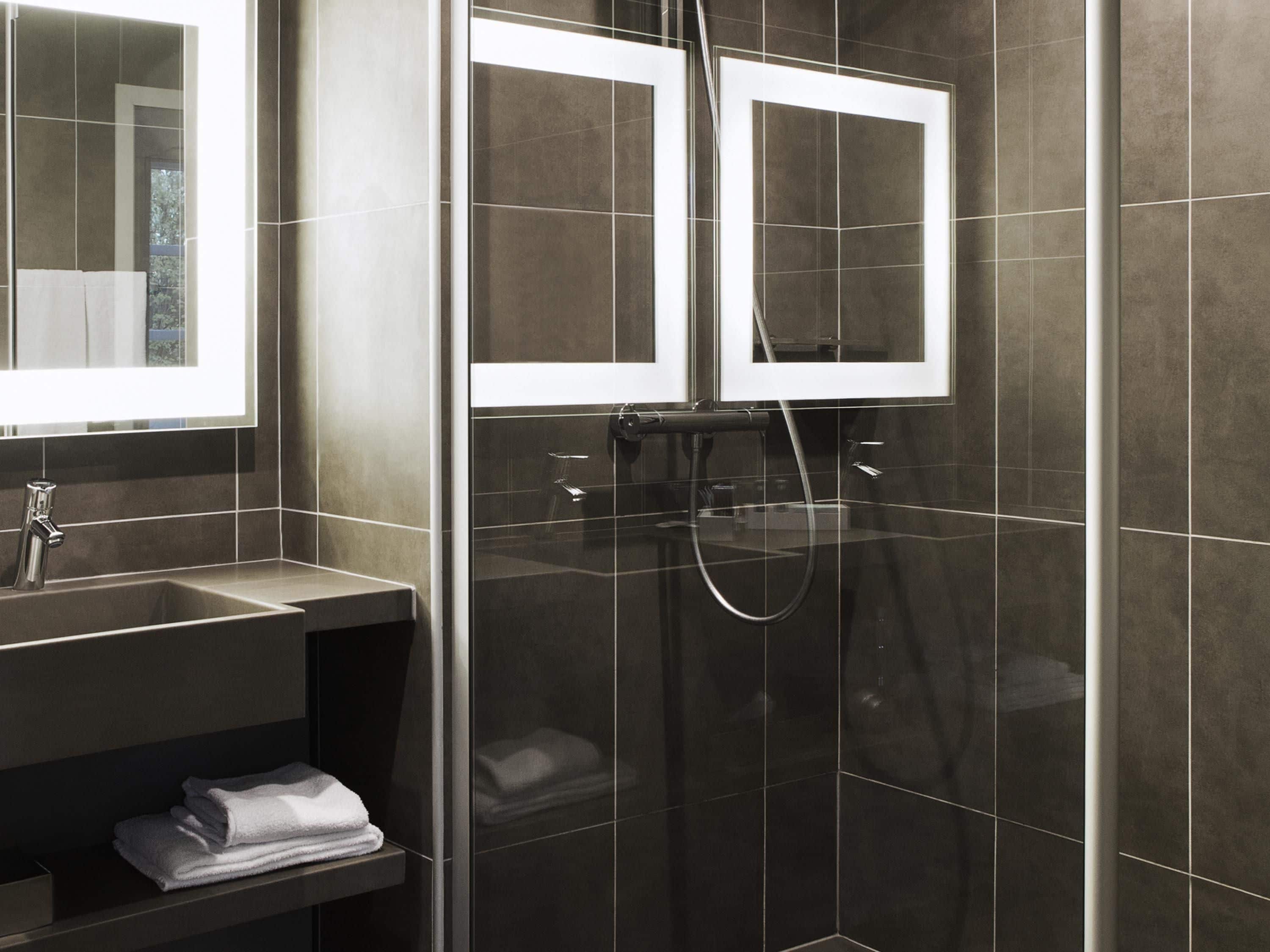 A modern bathroom with a glass-enclosed shower, a vanity with a mirror, and a shelf with folded towels.