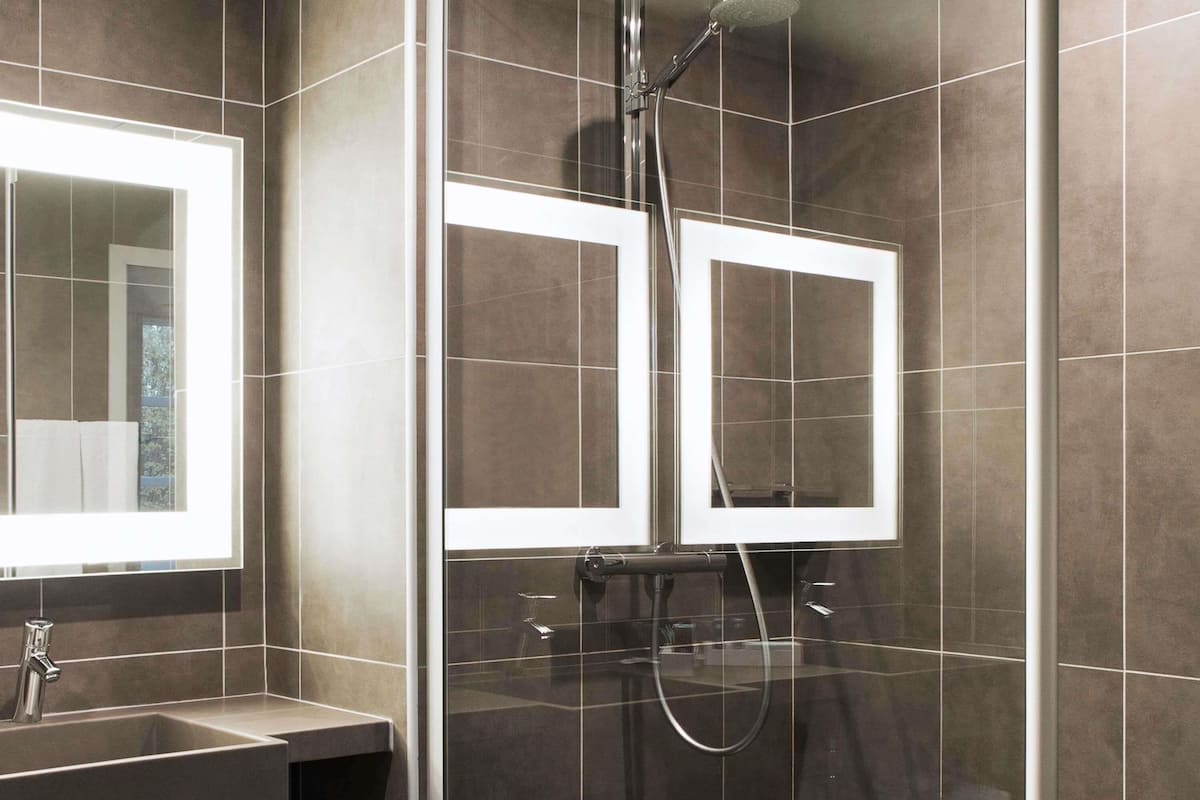 A modern bathroom with a glass-enclosed shower, a large mirror, and a sink.