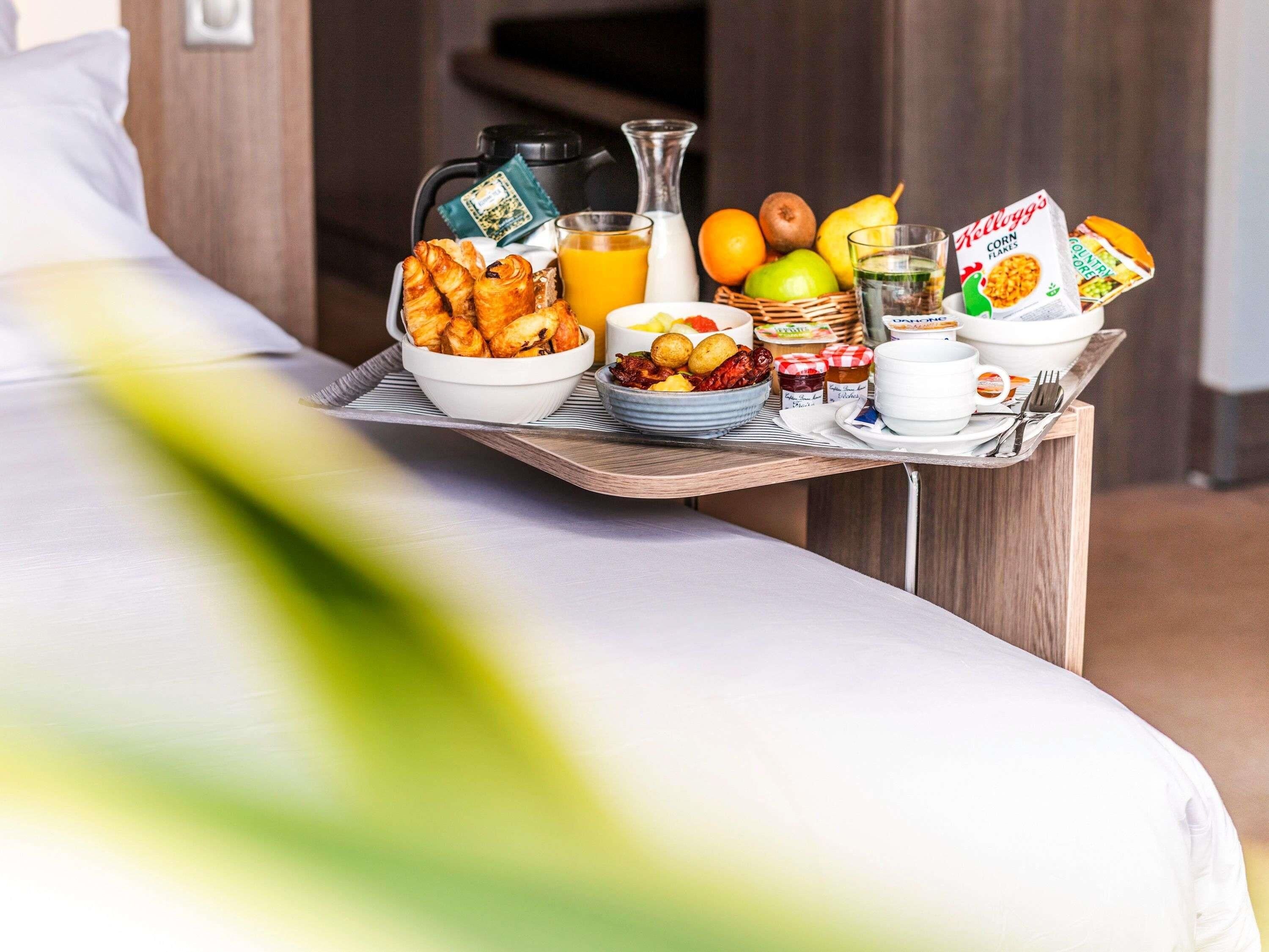 A breakfast tray with croissants, fruits, cereal, and beverages on a bed.