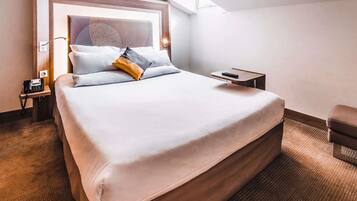 A hotel room with a large bed, a bedside table with a phone, a remote control, and a small chair.