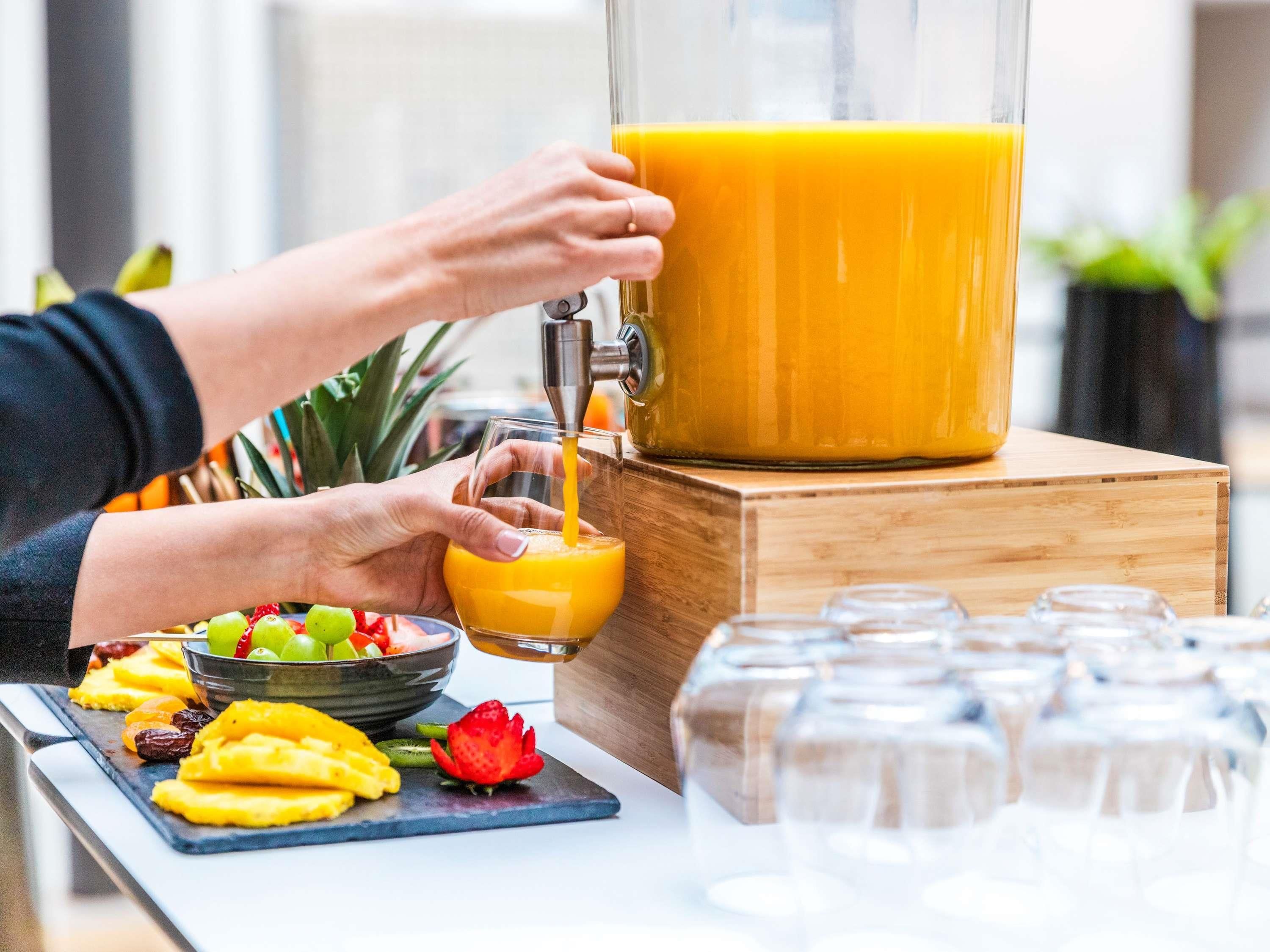 A person pouring orange juice from a large pitcher into a glass.