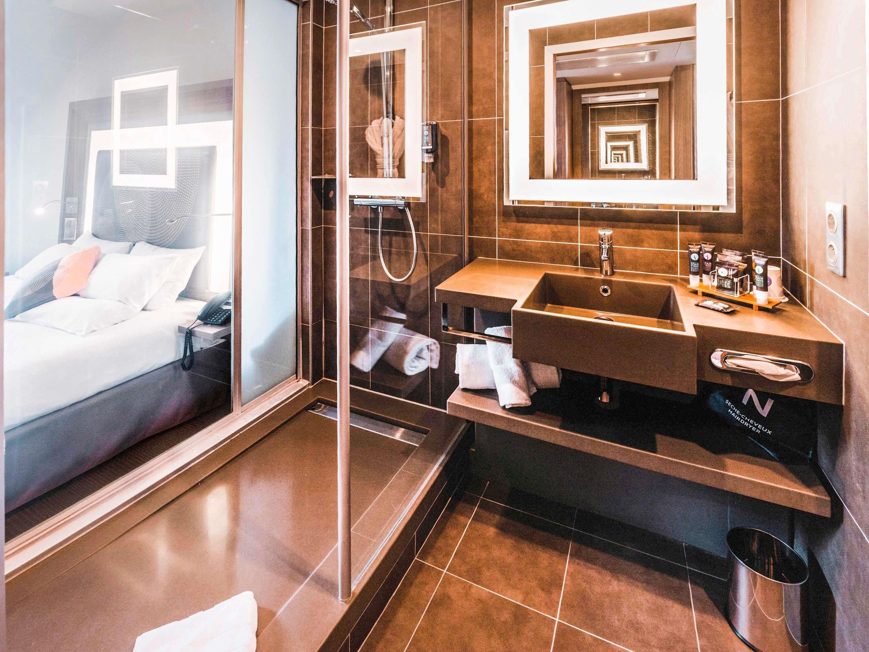 Una habitación de hotel moderna con una cama, un baño con un espejo grande, un lavabo y una ducha.