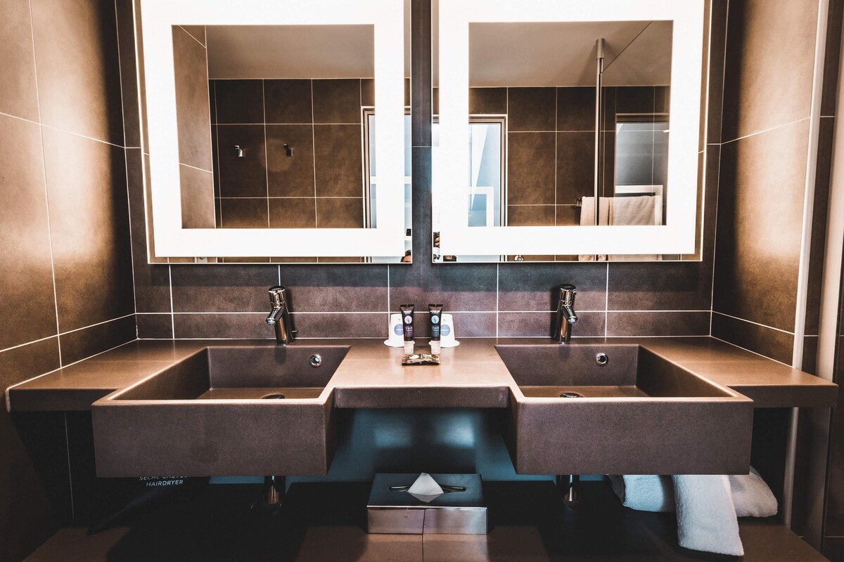 Une salle de bain moderne avec deux lavabos, de grands miroirs et un sèche-cheveux.