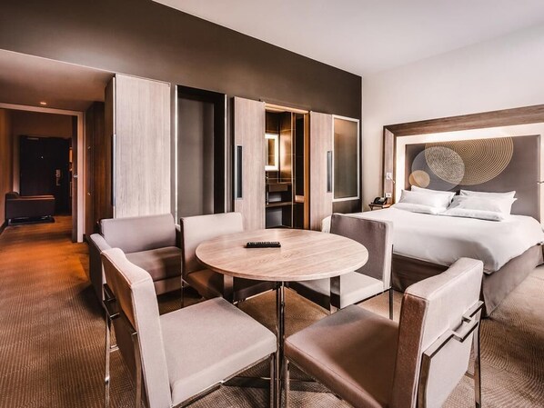 Ein Hotelzimmer mit Bett, einem runden Tisch mit Stühlen, einem Kleiderschrank und Blick auf den Flur.
