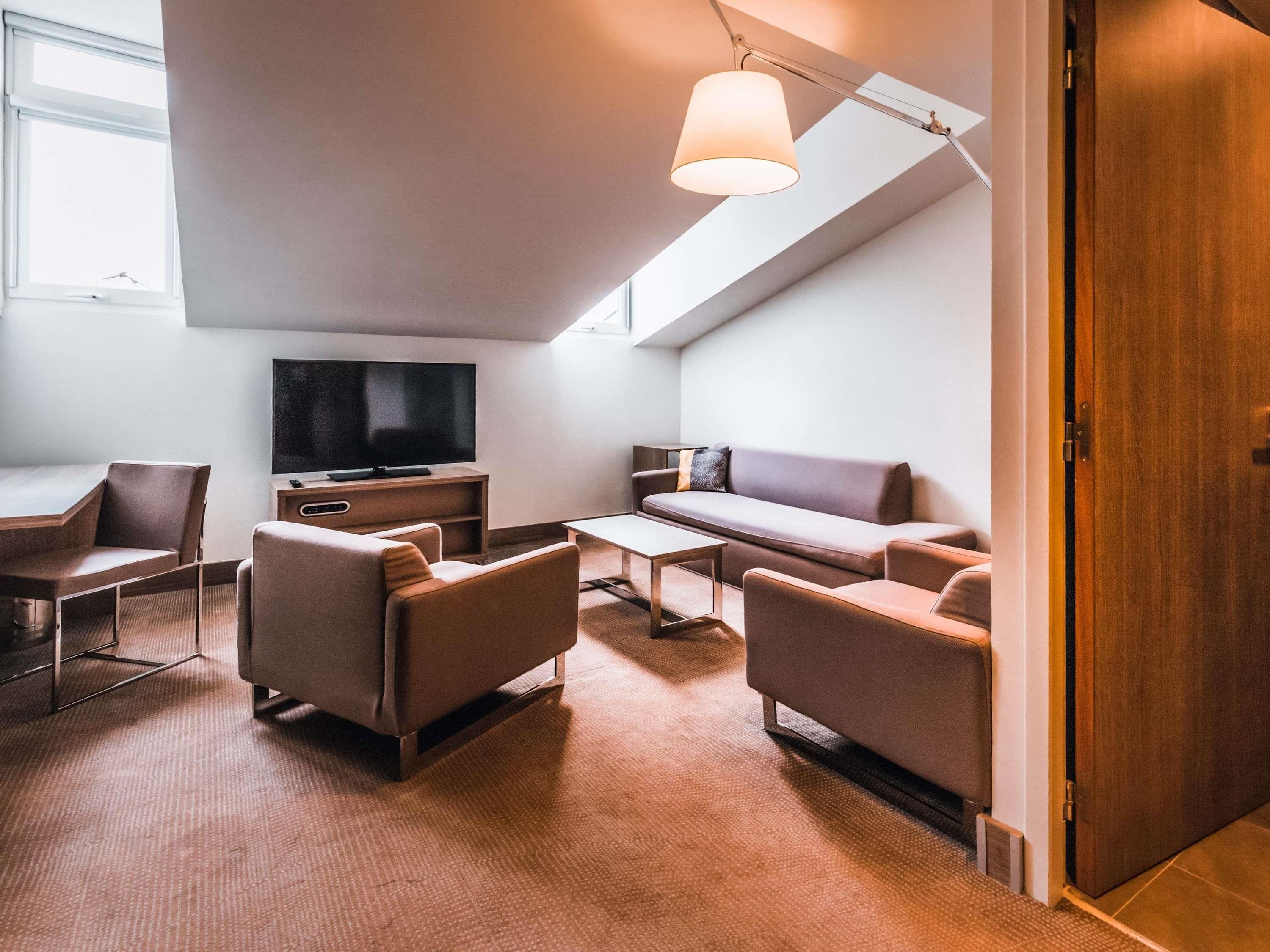 A modern living room with a flat-screen TV, sofa, chairs, and a ceiling light fixture.