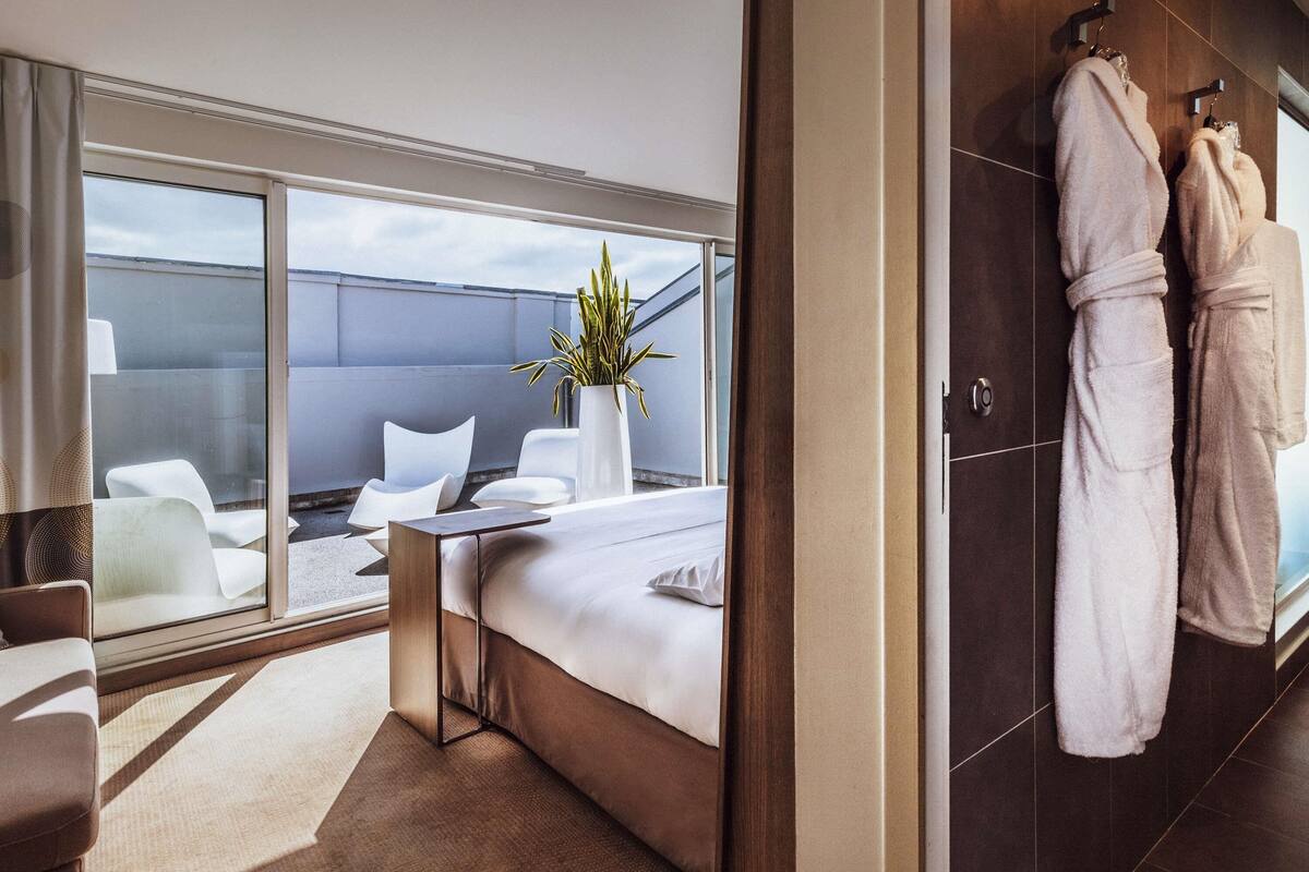 Een moderne hotelkamer met een groot bed, een zithoek met stoelen, een potplant en uitzicht op zee.