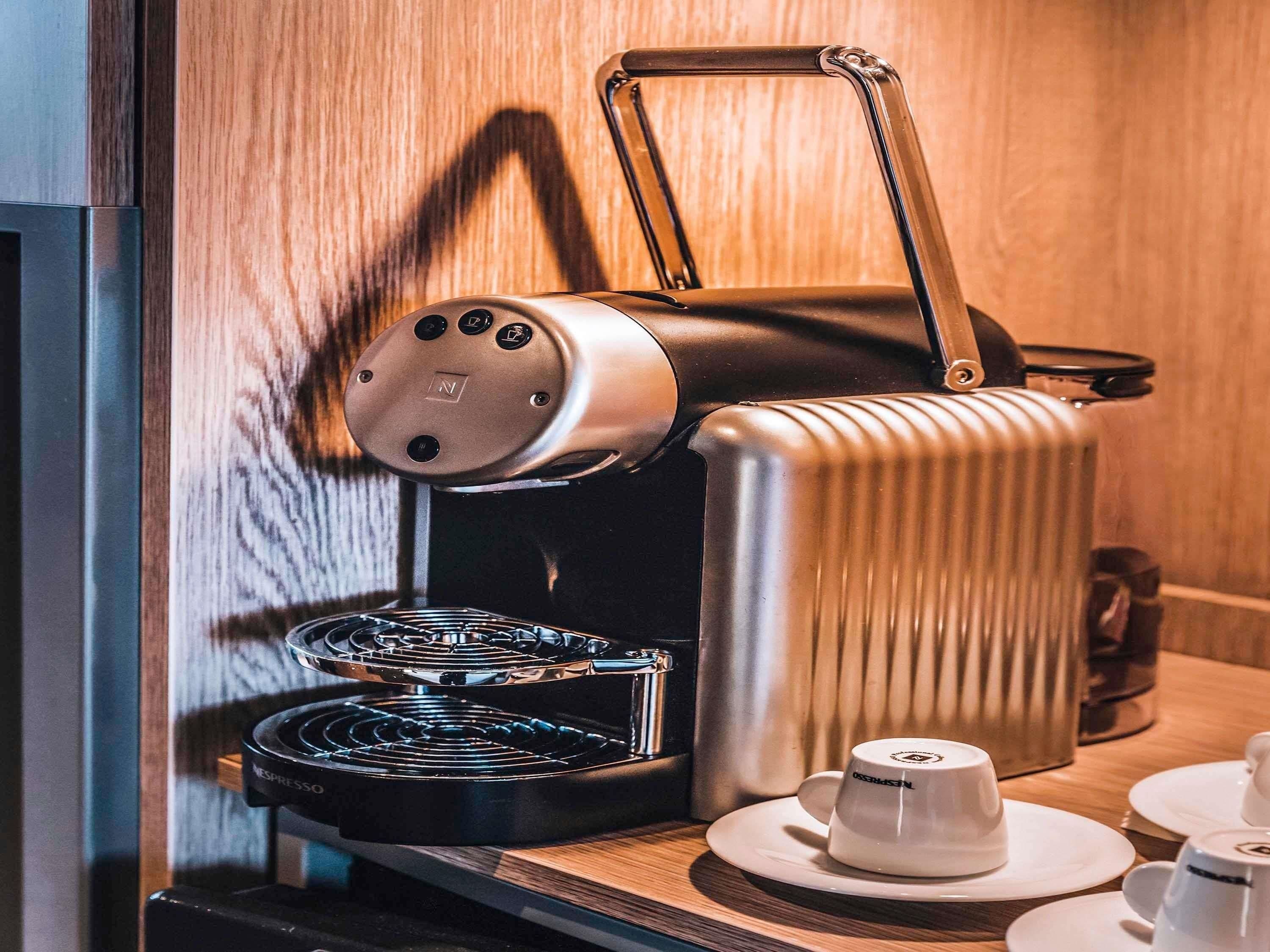 A Nespresso coffee machine with a water reservoir, a coffee pot, and a cup on a table.