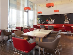 A modern restaurant with red and brown chairs, white tables, and a black wall with a fruit mural.