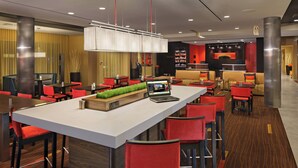 Un hall d'hôtel moderne avec un bar central, des sièges rouges et noirs et un comptoir d'accueil.