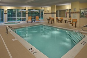 Ein Hallenbad mit klarem Wasser, einem Rettungsschwimmerstuhl und einem Hinweisschild für den Poolbereich.